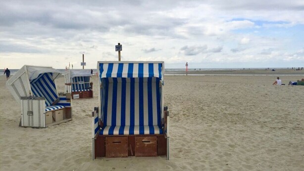 Beach chairs with striped cushions, a lifeguard tower, and a sandy beach. - Holiday Apartment Stork's Nest (Friedrichstadt)
