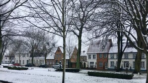 A snow-covered street with traditional European-style houses, a paved sidewalk, and a parked car. - Holiday Apartment Stork's Nest (Friedrichstadt)