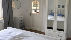 A bedroom with a bed, a wardrobe, a dresser, a mirror, and a door leading to another room. - Holiday Apartment Stork's Nest (Friedrichstadt)
