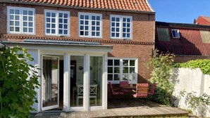 A two-story house with a patio area featuring a table and chairs, a sliding glass door entrance, and a small garden. - Holiday Apartment Stork's Nest (Friedrichstadt)