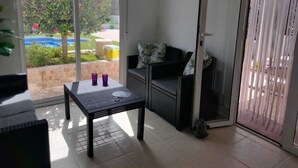 A room with a sliding glass door leading to a patio, a black wicker sofa, a small table with two purple cups, and a poster on the wall.