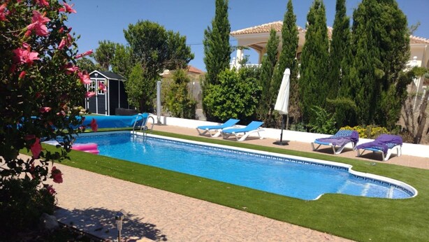 A swimming pool with a tiled deck, surrounded by green grass and trees.