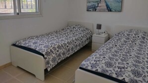 A bedroom with two beds, a window, and a painting of a pier.