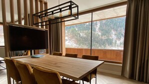 Un salón de conferencias moderno con una gran mesa, sillas cómodas, un televisor de pantalla plana y un amplio ventanal con vistas panorámicas a un área boscosa.