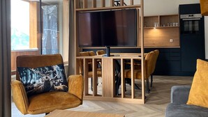 Un salón moderno con un televisor de pantalla plana grande, muebles de madera y una zona de cocina con horno empotrado.