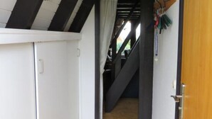 Een smalle gang met witte wanden, een houten deur en een trap naar een andere kamer.