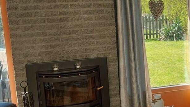 A cozy living room with a fireplace, a wooden coffee table, and a view of a garden through a window. - Arielle by the Sea Comfortable Holiday Residence (Julianadorp)