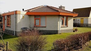A single-story house with a tiled roof, brick exterior, and a fenced yard. - Arielle by the Sea Comfortable Holiday Residence (Julianadorp)