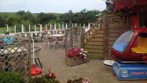 A wooden deck with outdoor seating, a small ride, and a flag. - Arielle by the Sea Comfortable Holiday Residence (Julianadorp)