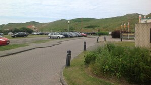 A parking lot with cars and a building with flags. - Arielle by the Sea Comfortable Holiday Residence (Julianadorp)