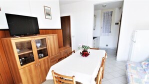 A dining area with a white table, wooden chairs, and a cabinet with a television. - Holiday Home in Rosolina Mare Near Beach (Rosolina)
