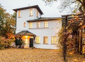 A two-story building with a covered patio and a garden area with fallen leaves. - Holiday Apartment in Werder (Werder (Havel))