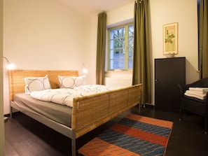 A bedroom with a bed, a window with curtains, a radiator, a chair, and a framed picture on the wall. - Holiday Apartment in Werder (Werder (Havel))