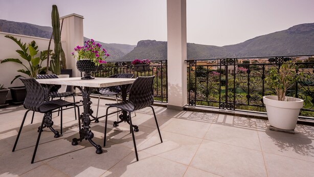 Um terraço com mesa e cadeiras, plantas em vasos e vista para montanhas.