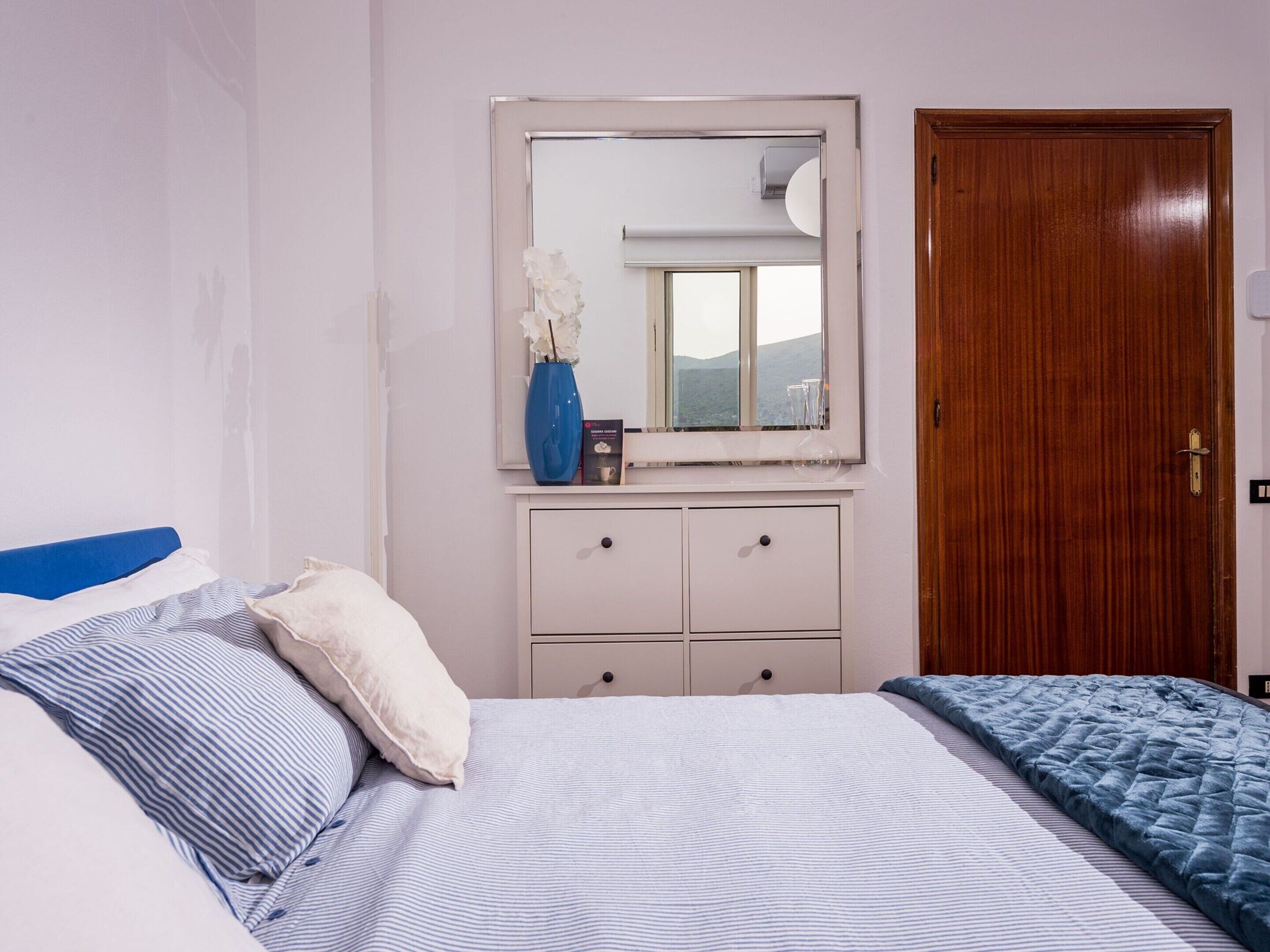 A bedroom with a bed, a dresser, a mirror, and a door.