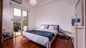 Quarto com cama, mesa de cabeceira, cómoda e porta de vidro deslizante que dá para uma varanda.