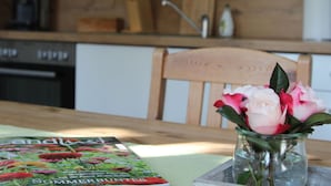 Una cocina con una mesa de madera, una revista y un jarrón con flores.