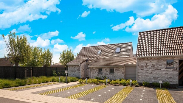 A building with a tiled roof, brick walls, and a paved parking area with tactile paving for visually impaired individuals. - Holiday Home in Koksijde With Private Garden (Koksijde)