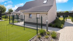 A small, single-story building with a tiled roof, surrounded by a green fence and a paved walkway. - Holiday Home in Koksijde With Private Garden (Koksijde)