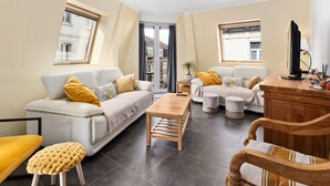 A modern living room with a sofa, ottoman, wooden coffee table, and a TV stand. - Beautiful Duplex Near Shopping Street (Blankenberge)