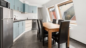 A modern kitchen with light blue cabinets, a stainless steel refrigerator, and a dining area with a wooden table and black chairs. - Beautiful Duplex Near Shopping Street (Blankenberge)