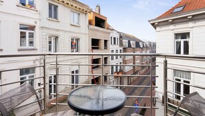 A balcony with a round table, overlooking a street with buildings. - Beautiful Duplex Near Shopping Street (Blankenberge)