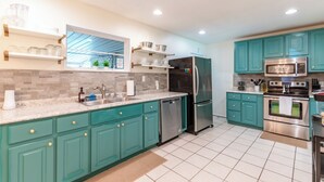 A modern kitchen with teal cabinets, stainless steel appliances, and a large window providing natural light. - Modern in the Magic City (Irondale)