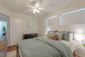 Une chambre à coucher comprenant un lit, un ventilateur de plafond, une table de chevet avec une lampe et une commode.