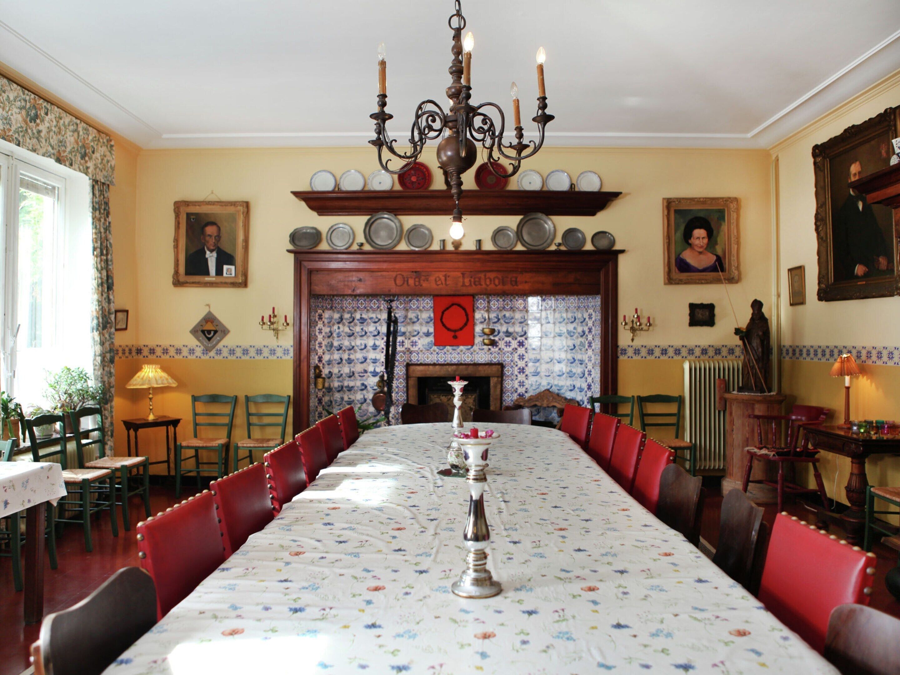 A dining room with a long table, red chairs, a chandelier, and a fireplace.