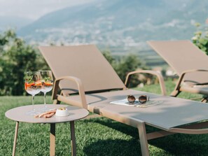 A table with two glasses of a beverage, a bowl of snacks, and a pair of sunglasses, set on a lawn with a view of mountains. - On the Slope Comfortable Holiday Residence (Cermes)