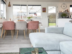 A modern living room with a grey sofa, pink chairs, and a dining area with a table and chairs. - 5 Person Holiday Home in Juelsminde (Horsens)