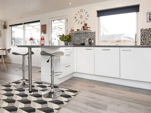 A modern kitchen with white cabinets, a black and white patterned rug, and a bar stool. - 5 Person Holiday Home in Juelsminde (Horsens)
