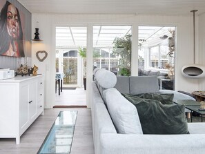 A modern living room with a sofa, a glass coffee table, and a view through a glass door to an outdoor area.