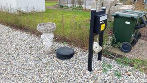 Une zone recouverte de gravier, avec une sculpture en pierre, un pneu noir et une poubelle verte.