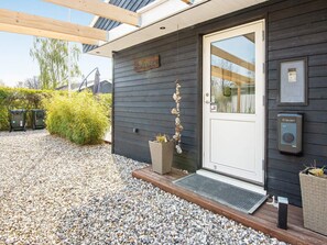 A modern building with a dark exterior, a white door, and a stone wall decoration. There are two trash bins and a Clever doorbell on the right side.