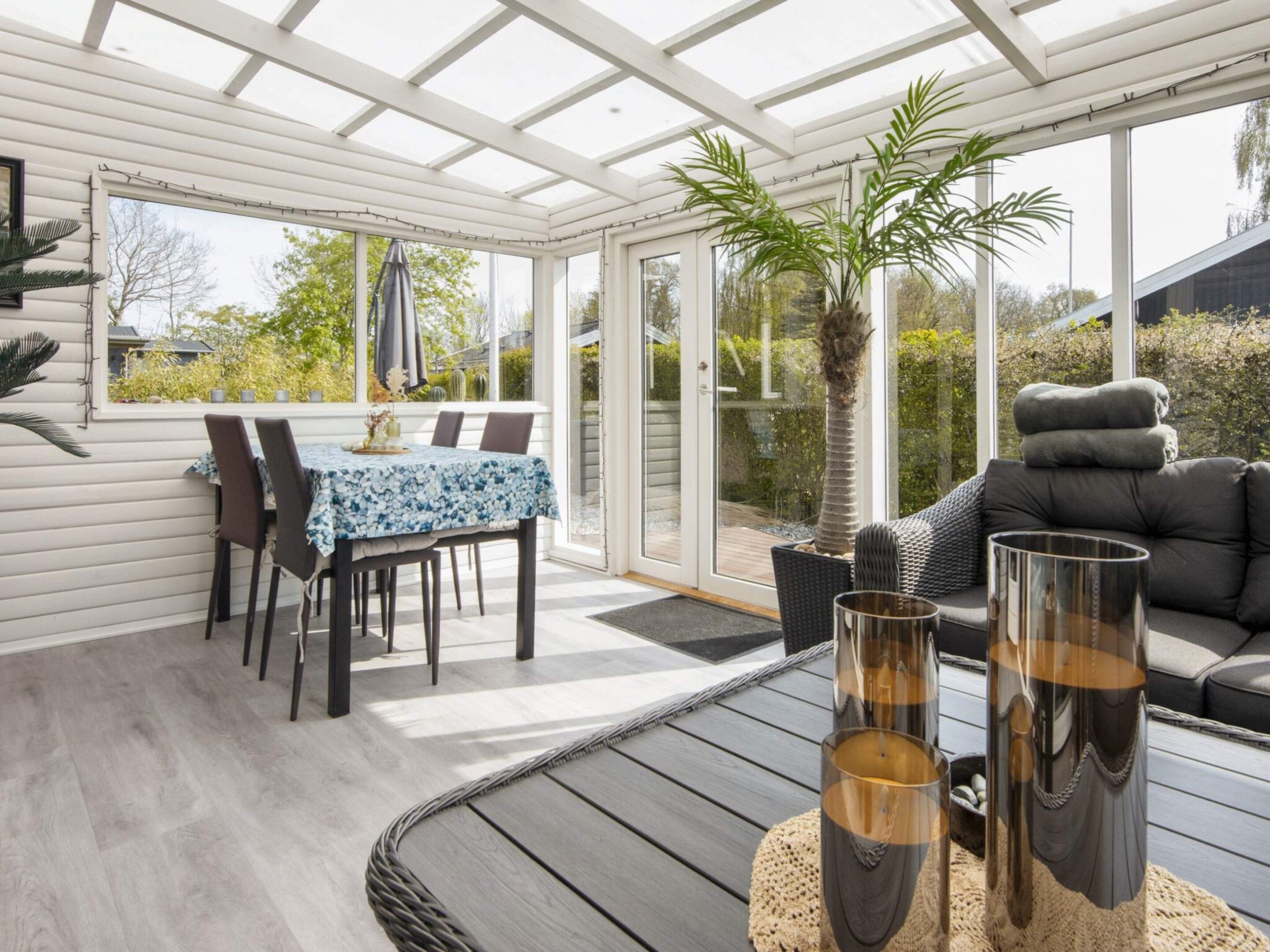 A sunroom with a dining table and chairs, a sofa, and a large window.