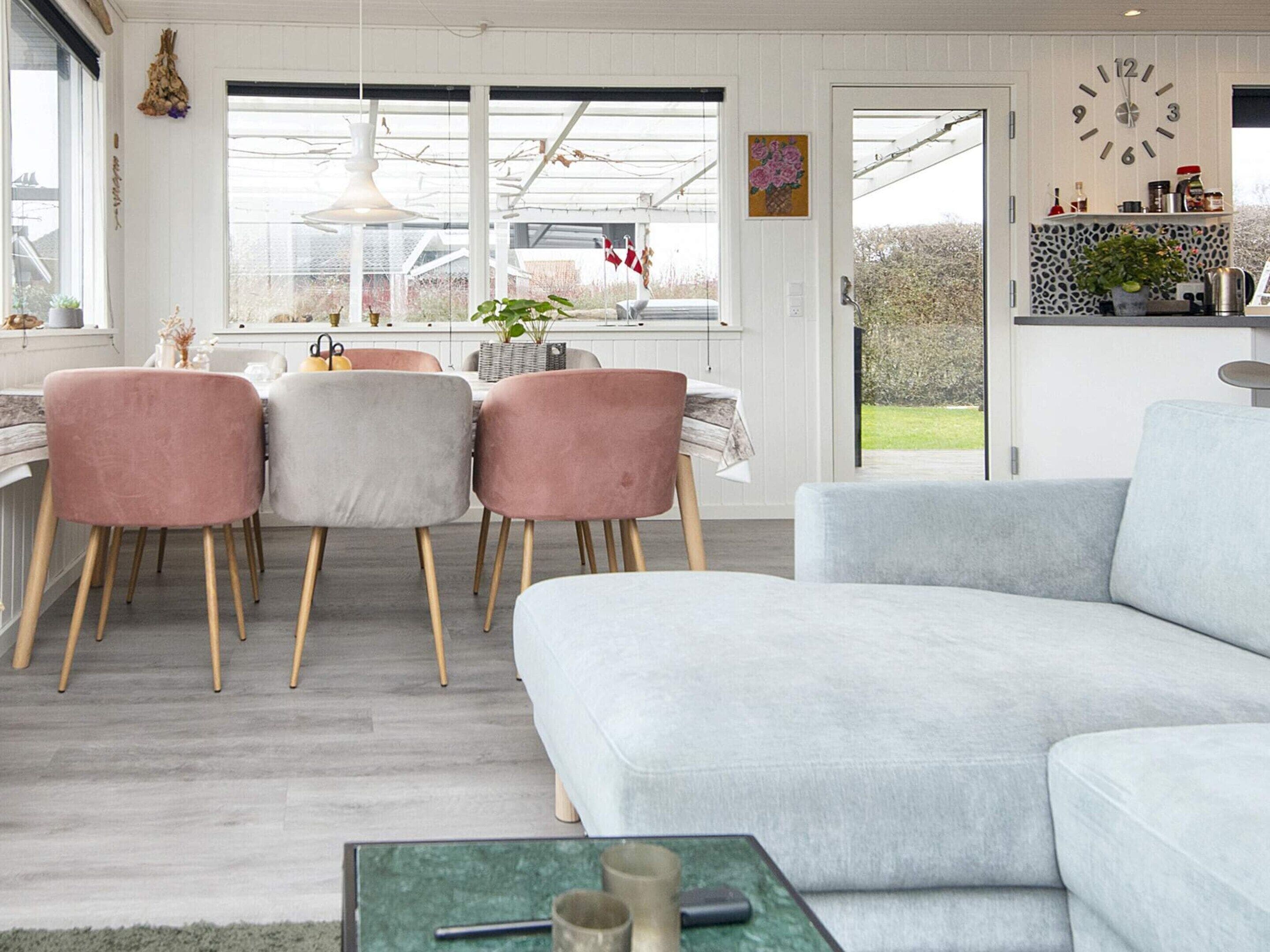 A modern living room with a grey sofa, pink chairs, and a dining area with a table and chairs.