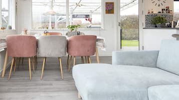 Un salon moderne avec un canapé gris, des fauteuils roses et un coin repas comprenant une table et des chaises.