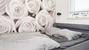 A bedroom with a bed, pillows, and a wall with a rose pattern.