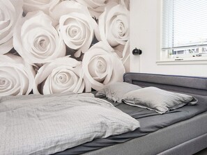 A bedroom with a bed, pillows, and a wall with a rose pattern.