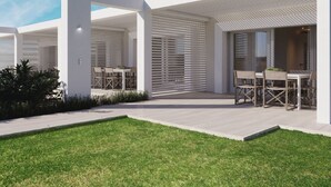 A modern outdoor patio area with white walls, large windows, and a grassy lawn. - Holiday Home in Stintino Near Iconic Beaches (Stintino)