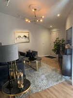 Una sala de estar moderna con un sofá, una mesa de centro y una lámpara. Hay un cuadro en la pared y una planta en la esquina.