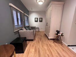 Una habitación con un sofá gris, un mueble negro, un armario blanco y una pequeña mesa con objetos encima.