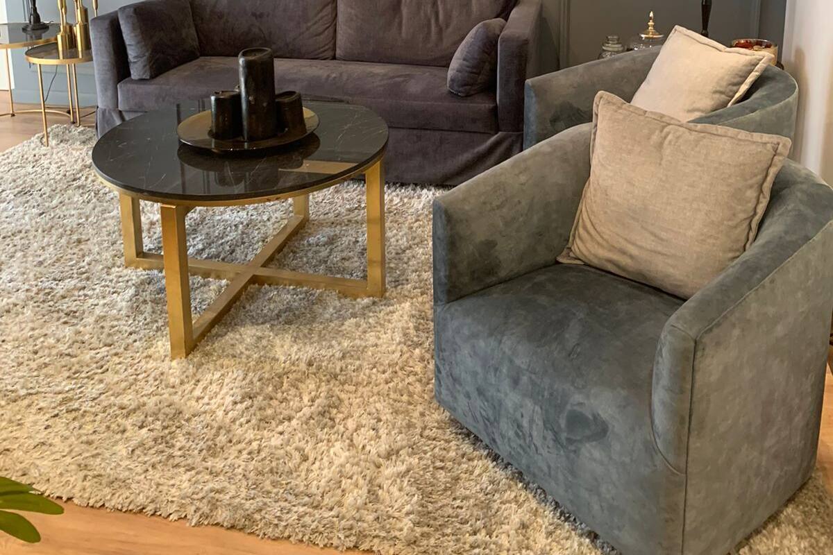 Una sala moderna con un sofá gris, una mesa de centro redonda y un sillón gris. Se observa un cuadro abstracto enmarcado en la pared y una lámpara sobre una mesita auxiliar.
