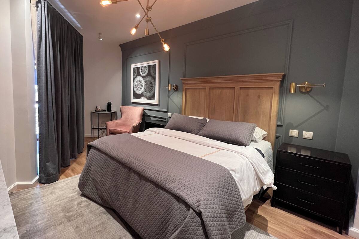Un dormitorio moderno con una cama grande, un cabecero de madera, un escritorio pequeño y una silla.