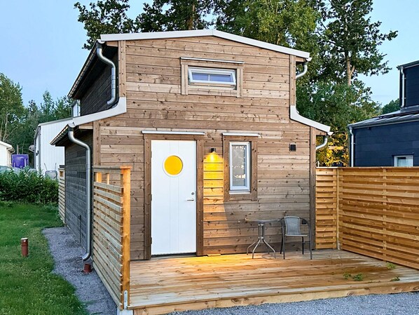 A wooden cabin with a front door, a small window, and a porch with a table and chair. - 4 Person Holiday Home in Farjestaden (Farjestaden)