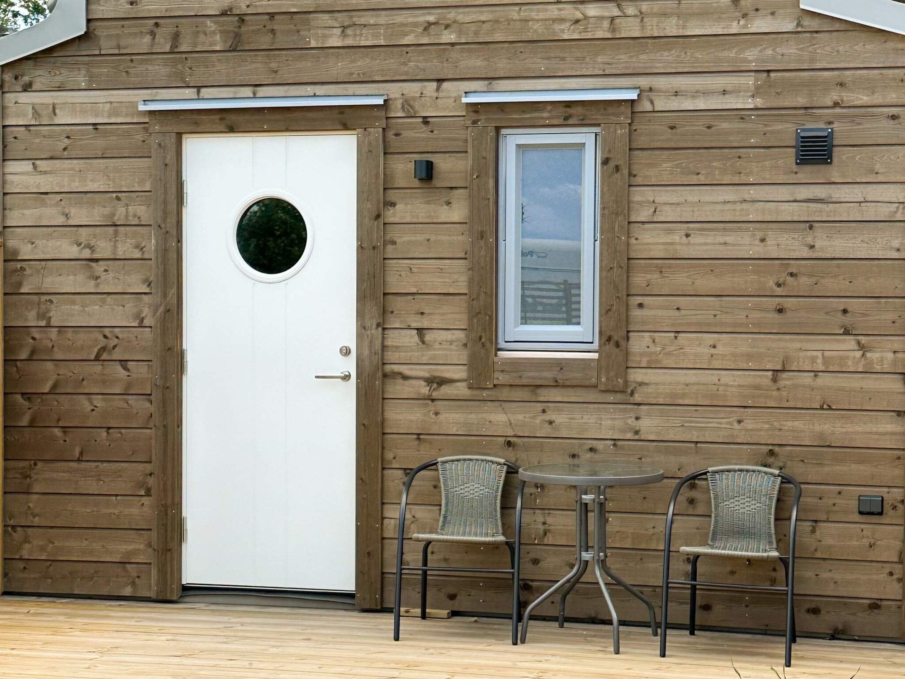 A wooden cabin with a white door, a small window, and two wicker chairs.