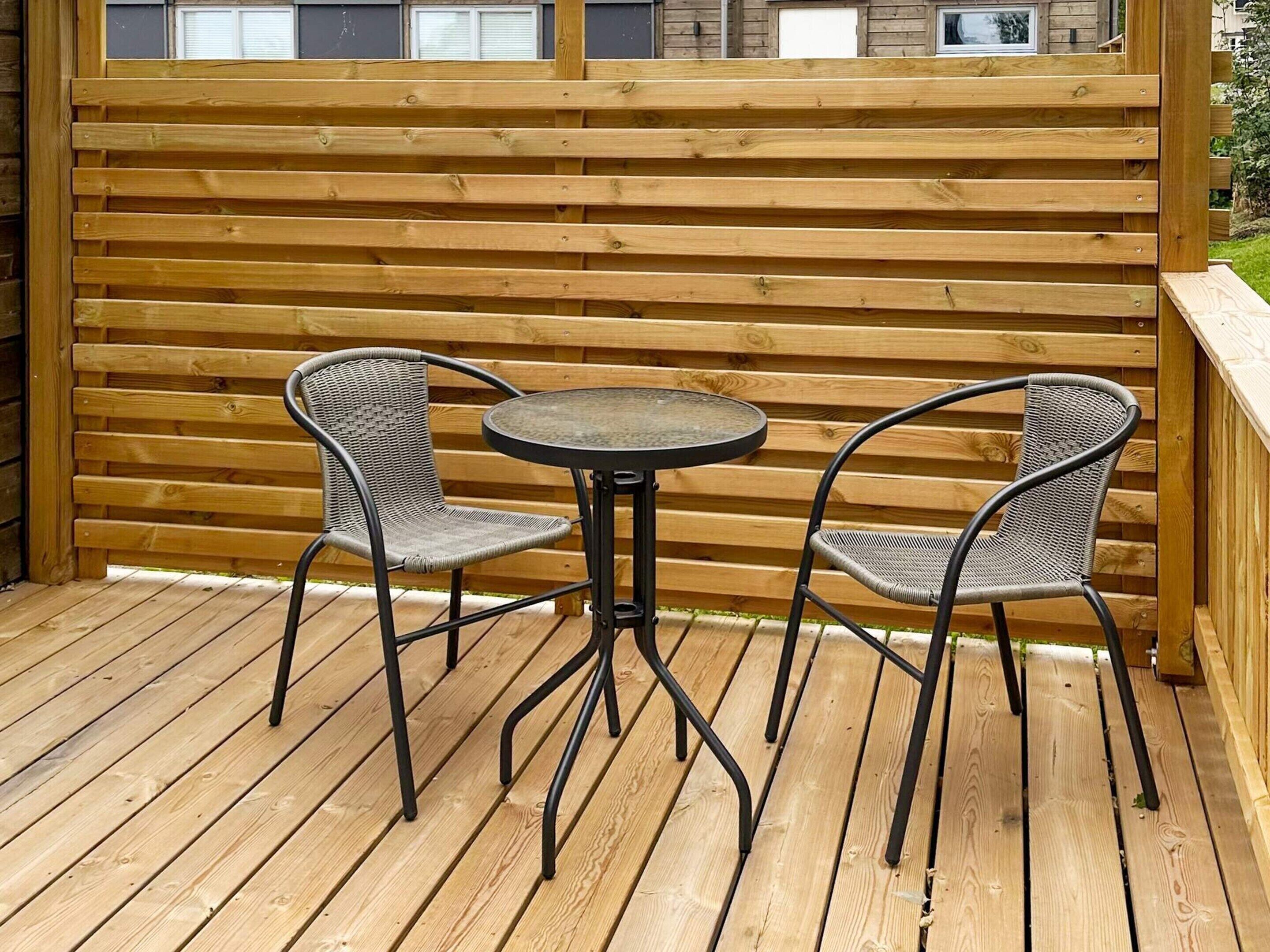 Een houten terras met twee rieten stoelen en een klein, rond tafeltje.