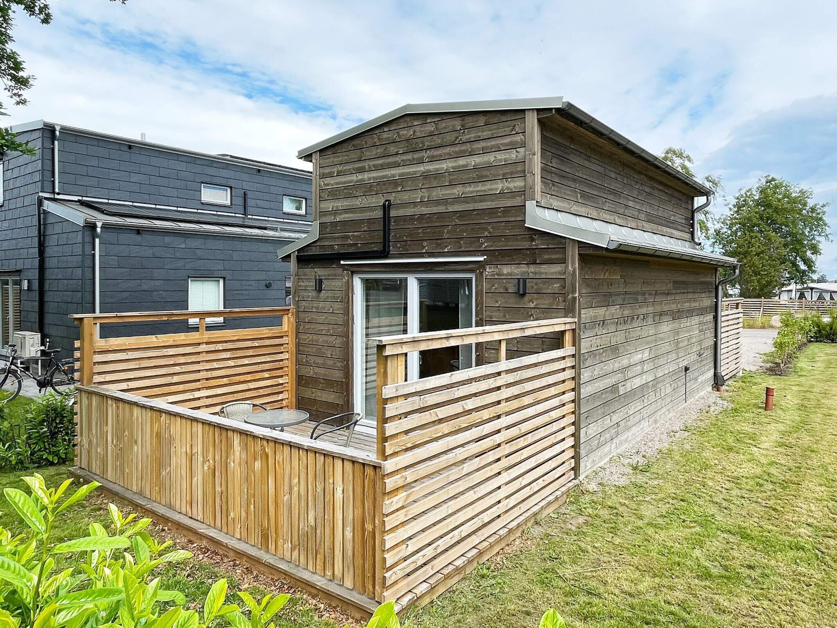A modern wooden cabin with a deck, a window, and a door.