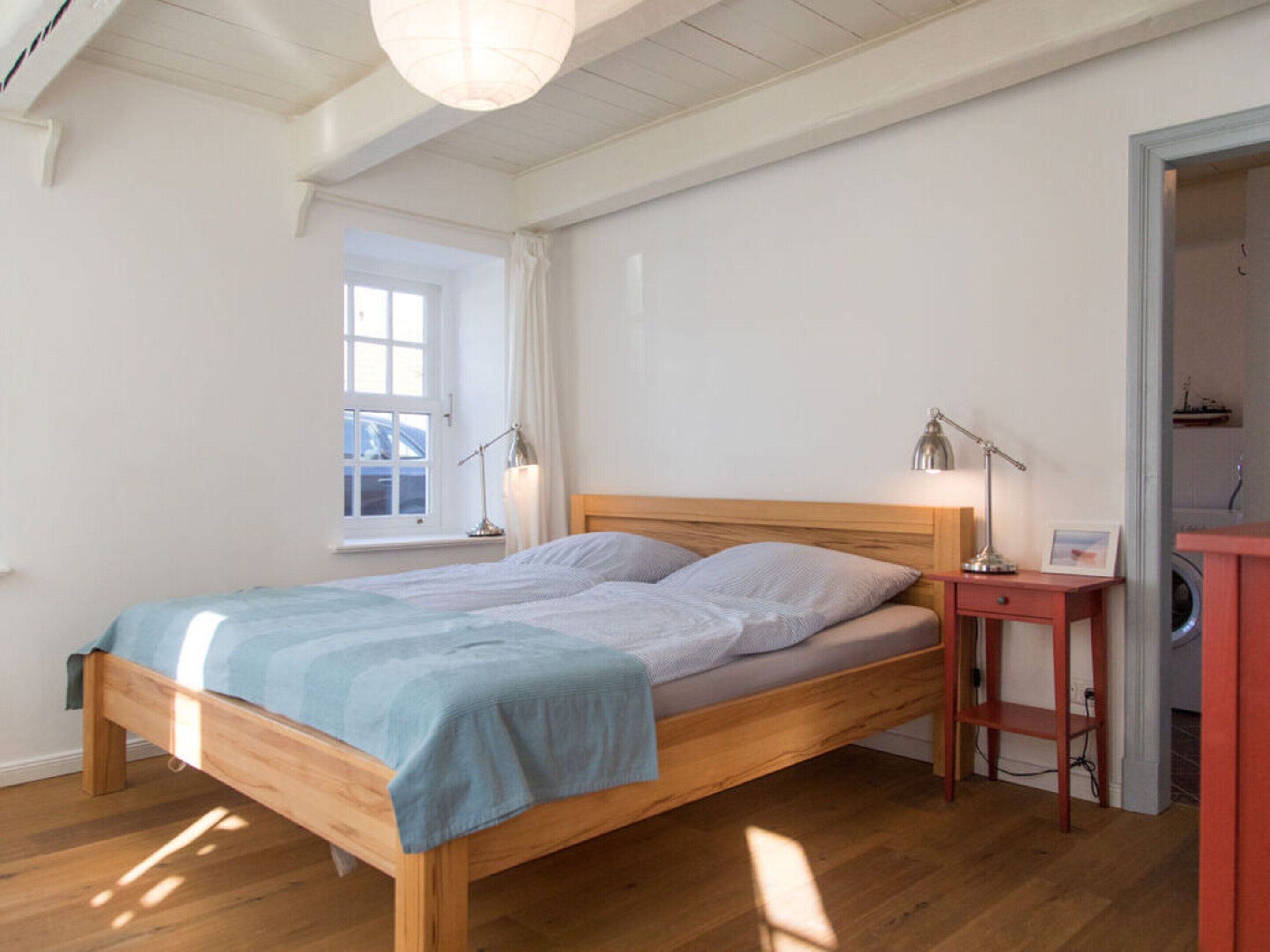 A bedroom with a wooden bed, two bedside lamps, a small wooden nightstand, and a window with curtains.